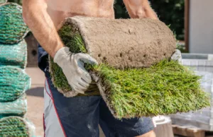 A worker carrying a fresh roll of grass turf during garden installation, showing the quality homeowners look for when they want to buy lawn turf for a new lawn.